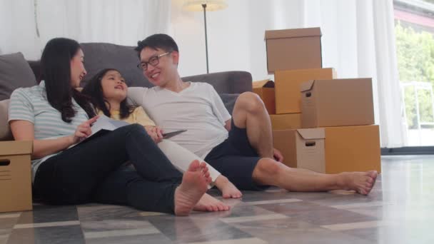 幸せなアジアの若い家族の住宅所有者は新しい家を買った 中国のお母さん お父さん お娘さんは 一緒に箱と床に座って移転した後 新しい家で将来を楽しみにしています — ストック動画