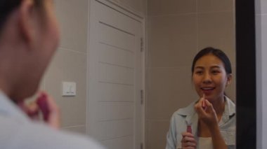Güzel Asyalı kadın aynanın önünde ruj kullanıyor, Mutlu Çinli kadın güzellik kozmetik kullanıyor ve kendini evdeki tuvalette çalışmaya hazırlıyor. Yaşam tarzı kadınları ev kavramında rahatlar