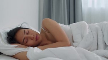 Asyalı Japon kadın evde uyuyor. Kendini mutlu hisseden Asyalı genç kız yatakta dinleniyor, rahat ve sakin hissediyor. 4k çözünürlük ve Yavaş çekim.