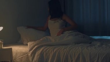 Güzel Asyalı genç bir kadın yatak odasında rahat rahat uyuyor. Hintli bir kadın, gece yarısı yatağın yanındaki ışık düğmesini kapatıyor ve uyumaya hazır. Tatlı rüyalar ve rahatlama konsepti.