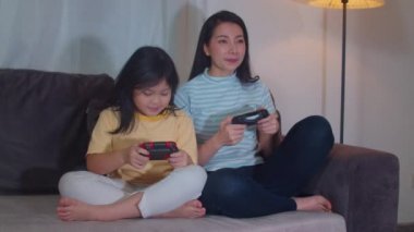 Genç Asyalı aile ve kız geceleri evde oyun oynuyorlar. Koreli bir anne ve küçük bir kız oturma odasındaki kanepede birlikte komik bir mutluluk anı geçiriyorlar. Komik anne ve güzel çocuk eğleniyor.