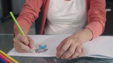 Genç Asyalı hamile kadın karnına ve ailesine not defterine bebek çiziyor. Babam karısının karnına dokunurken mutlu bir şekilde gülümsüyor, pozitif ve huzurlu bir şekilde. Bu arada evdeki oturma odasındaki masada çocuğuna bakıyor..