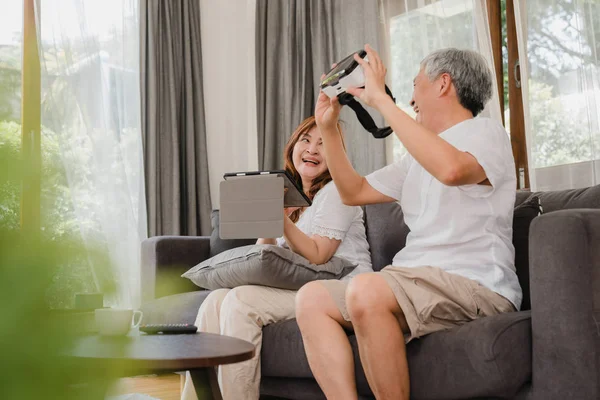 Asian elderly couple using tablet and virtual reality simulator playing games in living room, couple feeling happy using time together lying on sofa at home. Lifestyle Senior family at home concept. — Stock Photo, Image