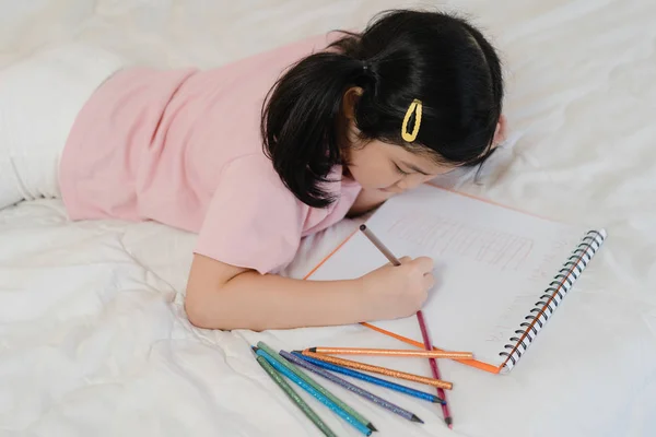 Young Asian girl drawing at home. Asia japanese woman child kid relax rest fun happy draw cartoon in sketchbook before sleep lying on bed, feel comfort and calm in bedroom at night concept. — Stock Photo, Image