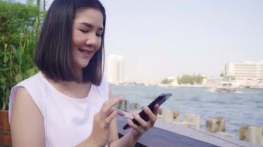 Açık kafede cep telefonu kullanan Asyalı turist kadınlar. Genç Japon Asyalı kız akıllı telefon kullanıyor sosyal medyayı kontrol ediyor ve sosyal ağdaki arkadaşlarıyla mesajlaşıyor tatilin tadını çıkarıyor..