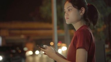 Genç gezgin Asyalı kadın, Bangkok 'ta bir gece eve cep telefonuyla gitmek için taksi çağırma başvurusunu kullanıyor. Öğrenci kız dışarıda dinlenirken internet üzerinden akıllı telefon sohbeti yapıyor..