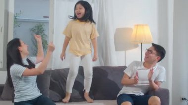 Mutlu genç Asyalı aile evdeki kanepede müzik dinleyip dans ediyor. Çekici Çinli anne baba ve kız çocuğu akşamları modern oturma odasında birlikte mutlu vakit geçiriyorlar..