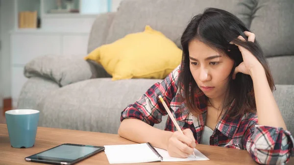 Mujer estudiante asiática hacer los deberes en casa, mujer usando tableta para buscar en el sofá en la sala de estar en casa. Estilo de vida de las mujeres relajarse en el hogar concepto. — Foto de Stock