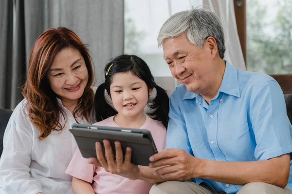 Asian grandparents and granddaughter video call at home. Senior Chinese, grandpa and grandma happy with girl using mobile phone video call talking with dad and mom lying in living room at home. — Stock Photo, Image