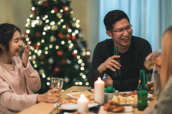 Hyvää joulua ja onnellista uutta vuotta! Nuoret ystävät syövät päivällistä kotona. Aasialaiset perhejuhlat oluella ja pizzalla lähellä joulukuusi talossa yöllä. Juhlaloma ja yhdessäolo . — kuvapankkivalokuva