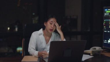 Millennial genç Çinli iş kadını küçük modern ofisteki toplantı odasında dizüstü bilgisayardaki proje araştırma sorunuyla geç saatlere kadar çalışıyor. Asyalıların mesleki tükenme sendromu. Yavaş çekim