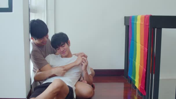 アジアのゲイのカップルが横になり 自宅で床にしがみついています 若いですアジアのLgbtq 男性接吻幸せなリラックスした休息一緒に過ごすロマンチックな時間でリビングルームに虹の旗とともに現代の家で朝 — ストック動画