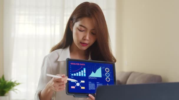 아시아 사업가는 집에서 거실에서 일하는 노트북과 태블릿 프레젠테이션을 사용하여 동료들에게 — 비디오