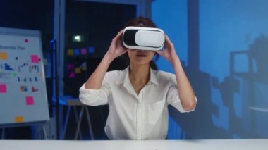 Genç Asyalı tasarımcı kadın video gözlük (sanal gerçeklik) kullanarak modern yaratıcı ev ofis gecesinde geliştirilen yazılımlardan mobil uygulamayı test ediyor. Corona virüsünün önlenmesi için sosyal mesafe ve karantina.