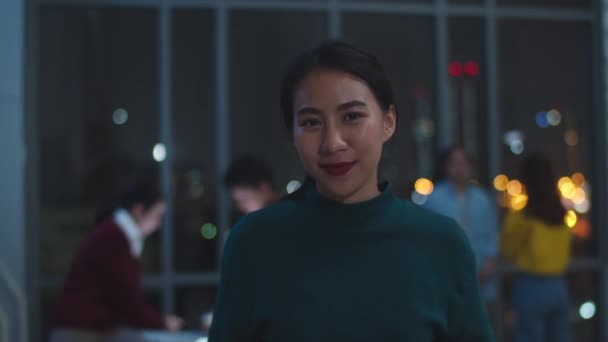 Porträt einer erfolgreichen Geschäftsfrau in eleganter Freizeitkleidung, die in die Kamera blickt und lächelt, glücklich in einem modernen Nachtbüro-Arbeitsplatz. Junge Asiatin steht entspannt im modernen Besprechungsraum.