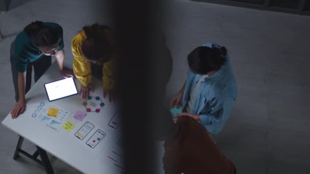 Groupe de jeunes créatifs asiatiques en vêtements décontractés intelligents discuter affaires brainstorming idées de réunion projet de conception de logiciels d'application mobile dans le bureau de nuit moderne. Concept de travail d'équipe entre collègues.