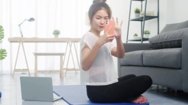 Spor kıyafetlerindeki genç bayan spor yapıyor hafif halterlerle spor yapıyor ve evdeki oturma odasında selfie çekiyor. Sosyal mesafe, virüs sırasında izolasyon, evde kal..