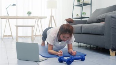 Egzersiz sonrası yorgunluk. Genç Koreli bayan egzersizleri yapıyor ve evde yoga videoları izlemek için dizüstü bilgisayar kullanıyor. Kişisel antrenörle uzak eğitim, sosyal mesafe.
