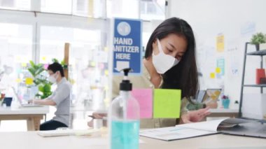 Asya 'lı iş kadını girişimci, ofiste dizüstü bilgisayar kullanırken virüsün önlenmesi için sosyal mesafeye tıbbi yüz maskesi takıyor. Coronavirüs 'ten sonra hayat ve iş.