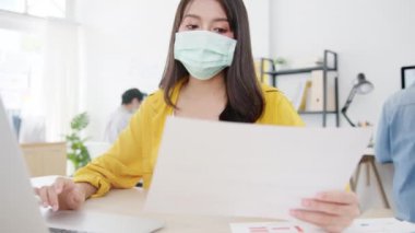 Asya 'lı iş kadını girişimci, ofiste dizüstü bilgisayar kullanırken virüsün önlenmesi için sosyal mesafeye tıbbi yüz maskesi takıyor. Corona virüsünden sonra yaşam tarzı.