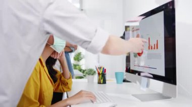 Asyalı iş adamları bilgisayar sunumu toplantısını kullanarak yeni proje arkadaşlarıyla ilgili fikir alışverişinde bulunuyor ve yeni normal ofiste koruyucu yüz maskesi takıyorlar. Coronavirus 'tan sonra yaşam tarzı ve çalışma.