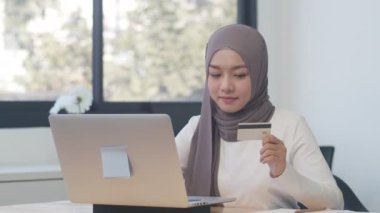 Bilgisayarı, kredi kartını ve e-ticaret internetini kullanan Asyalı Müslüman kadın. Evde kal, online alışveriş, kişisel izolasyon, sosyal uzaklık, koronavirüs önleme için karantina.