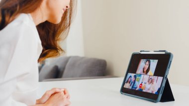 Genç Asyalı iş kadını, evde oturma odasında çalışırken ailesiyle konuşurken tablet video kullanıyor. Kişisel izolasyon, sosyal uzaklık, bir sonraki normal konseptte koronavirüs için karantina.