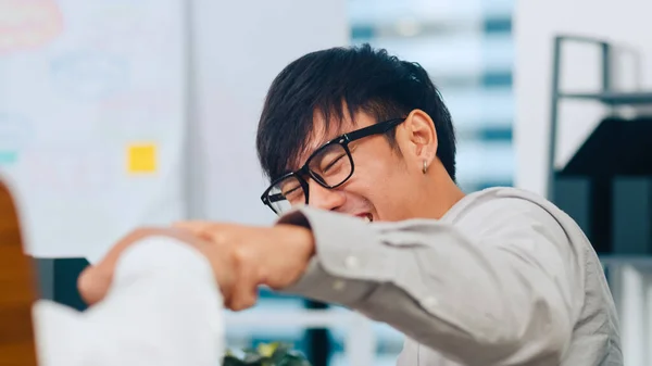 Asia young businessmen smart casual wear colleagues fist bumping celebrating successful teamwork friendly happy motivated coworker excited by good work result congratulating at meeting room in office.