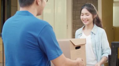Genç posta kuryesi, paketleri müşteriye göndermek için elinde tutuyor. Asyalı kadınlar, açık hava paketleri almak için cep telefonlarında QR kodu ile imza atıyor ve ödeme yapıyorlar..