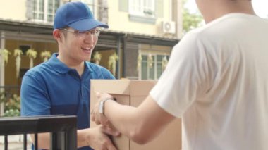 Genç posta kuryesi, paketleri müşteriye göndermek için elinde tutuyor. Asyalı erkekler, açık hava paketleri almak için cep telefonunda QR kodu ile imza atıyor ve ödeme yapıyor..