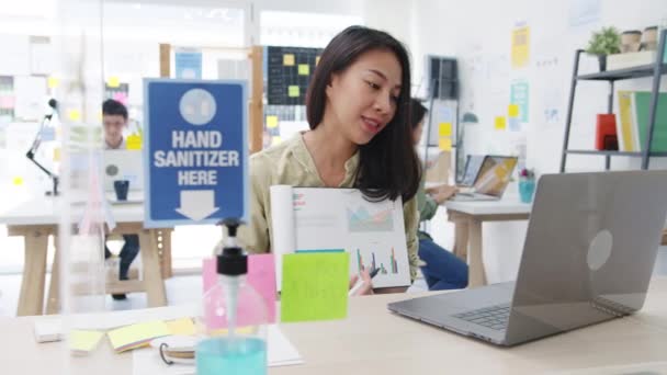 亚洲女商人在新的正常情况下与社会保持距离 以预防病毒 同时使用笔记本电脑向同事介绍在办公室工作时的视频通话计划 电晕病毒后的生命 — 图库视频影像