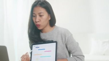 Asyalı iş kadını, yatak odasında çalışırken iş arkadaşlarına bilgisayar ve tablet sunumu yapıyor. Kişisel izolasyon, sosyal uzaklık, korona virüsü için karantina.