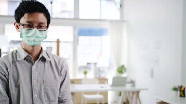 アジア男性受付担当者は オフィスに入る前にお客様の額に赤外線温度計チェッカーや温度銃を使用して保護顔マスクを着用します コロナウイルスの後のライフスタイルの新しい正常な — ストック動画