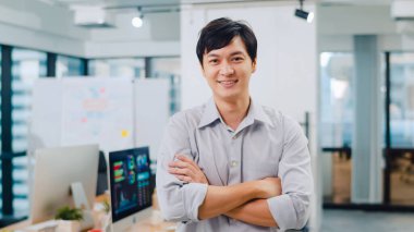 Modern ofis işyerinde kollarını kavuşturarak kameraya bakıp gülümseyen başarılı, yakışıklı yönetici iş adamının portresi. Genç Asyalı adam çağdaş toplantı odasında duruyor..