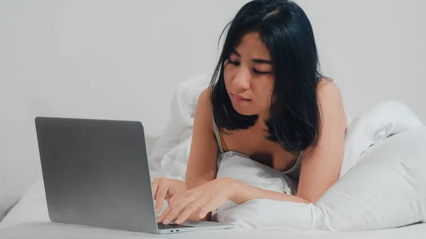 若いですアジアの女性を使用してノートパソコンをチェックソーシャルメディア感幸せな笑顔ベッドの上に横たわっながら 朝の家で目を覚ます 魅力的なタイの女の子笑顔リラックスでベッドルームに自宅のコンセプト — ストック写真