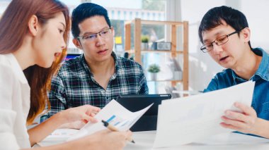 Mutlu genç Asyalı iş adamları ve iş kadınları yeni evrak işleri hakkında fikir alışverişinde bulunuyorlar. İş arkadaşları birlikte çalışıyorlar. Başarı stratejisi planlıyorlar..