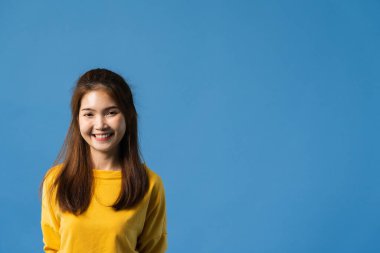 Olumlu ifadeli genç Asyalı bayan, geniş bir gülümseme, günlük kıyafetler giymiş ve mavi arka plandan kameraya bakıyor. Mutlu, sevimli, mutlu kadın başarıya sevinir. Yüz ifadesi kavramı.