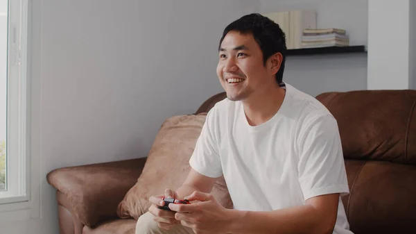 年轻的亚洲男人在客厅里用操纵杆玩电视游戏 男人在家里躺在沙发上放松一下 感觉很开心 男人在家里玩游戏放松 — 图库照片