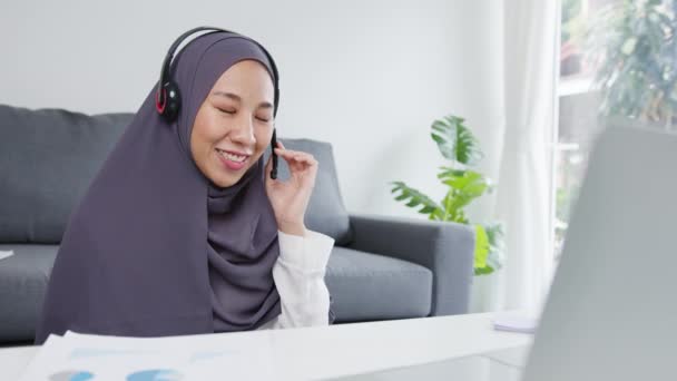 亚洲穆斯林女士在客厅工作时 带着耳机 用笔记本电脑和同事们谈论会议视频通话中的计划 社会疏离 为预防日冕病毒进行检疫 — 图库视频影像