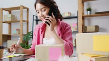 Genç Asyalı iş kadını cep telefonuyla arıyor satın alma emri alıyor ve ürünleri hisse senetlerinde kontrol ediyor, ev ofisinde çalışıyor. Küçük işletme sahibi, çevrimiçi pazar teslimatı, yaşam tarzı serbest konsepti.