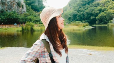 Sırt çantalı Asyalı neşeli genç gezgin bayan dağ gölünde yürüyor. Koreli genç kız mutlu bir özgürlük hissederek tatil macerasının tadını çıkarıyor. Yaşam tarzı seyahati ve boş zaman konseptinde rahatlama.