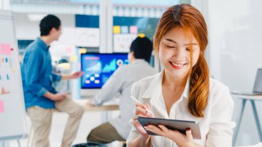 Dijital tablet kullanan Asyalı genç iş kadını iş arkadaşlarıyla video görüşmesinde planlar hakkında konuşurken modern ofisten akıllı bir şekilde çalışıyor. Bilgi teknolojisi, yerel yaşam tarzı veya uzaktan çalışma konsepti.