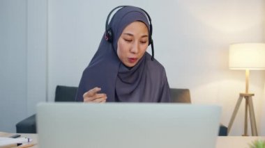 Asyalı müslüman kadın kulaklık takıyor. Webinar, internet üzerinden konferans videosuyla iletişim kuruyor. Evden, sosyal mesafeden, korona virüsünü karantinadan uzak tutmak.