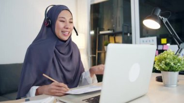 Asyalı müslüman kadın kulaklık takıyor. Webinar, internet üzerinden konferans videosuyla iletişim kuruyor. Evden, sosyal mesafeden, korona virüsünü karantinadan uzak tutmak.