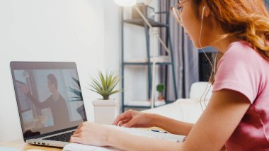 Genç Asya 'lı kız öğrencilerin arka planda kulaklık takması, internet öğretmeniyle uzaktan öğrenme dersi alması ve evde bilgisayar ekranında ders çalışması. Corona virüsünün önlenmesi için sosyal mesafe ve karantina.