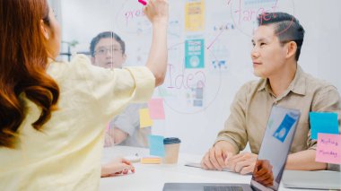 Asyalı iş adamları iş beyin fırtınası toplantısını tartışıyor verileri paylaşıyor ve yeni normal ofiste akrilik bölünme standı üzerine yazıyor. Yaşam tarzı sosyal uzaklık ve Coronavirüs 'ten sonra çalışma.