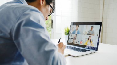 Genç Asya 'lı iş adamı, iş yerinde evden oturma odasına geçerken iş arkadaşlarıyla görüntülü görüşme planları hakkında konuşuyor. Kişisel izolasyon, sosyal uzaklık, korona virüsünün önlenmesi için karantina.