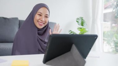 Asyalı Müslüman kadın, evde çalışırken konferans görüntülü konuşmasında meslektaşlarına satıştan bahsederken türban takıyor. Corona virüsü için sosyal uzaklık, karantina.