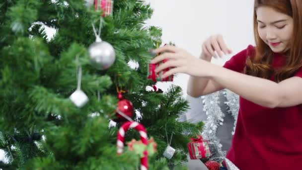 自宅のリビングルームでクリスマスツリーと新年祭でクリスマスツリー上の装飾で飾られたアジアの女性 クリスマスのお祝いイベント準備や冬の休日祭り屋内パーティーのコンセプト — ストック動画