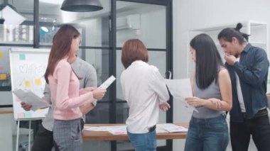 Bir grup Asyalı yaratıcı genç, gündelik akıllı insanlar kameraya bakıp yaratıcı ofis işyerinde gülümsüyorlar. Başlangıçta çeşitli Asyalı erkek ve dişiler birlikte dururlar. İş arkadaşı takım çalışması konsepti.